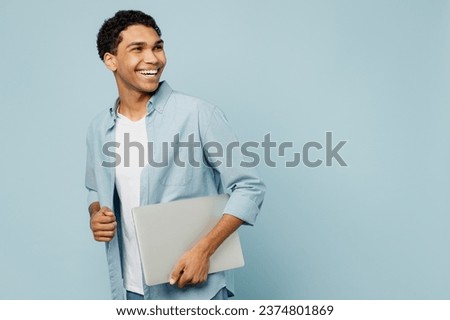 Side view young IT man of African American ethnicity he wear shirt casual clothes hold closed laptop pc computer hold use work on laptop pc computer look aside isolated on plain pastel blue background