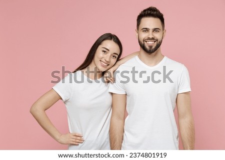 Young cheerful couple two friends bearded man brunette woman in white basic blank print design t-shirts posing looking camera standing smiling isolated on pastel pink color background studio portrait