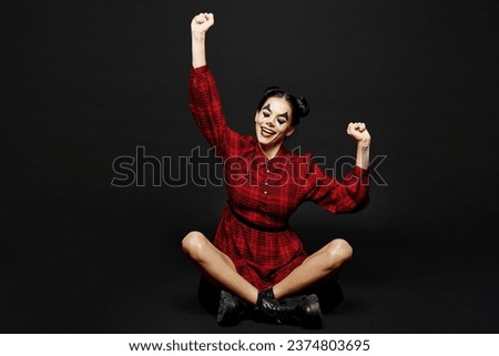 Full body young woman with Halloween makeup face art mask wear clown costume red dress sit do winner gesture celebrate clenching fists isolated on plain black background. Scary holiday party concept