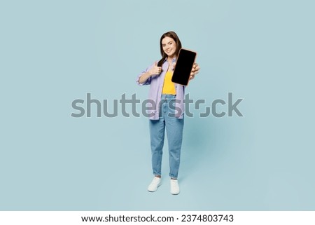 Full body young happy woman wears purple shirt yellow t-shirt casual clothes hold in hand use mobile cell phone with blank screen workspace area isolated on plain pastel light blue background studio