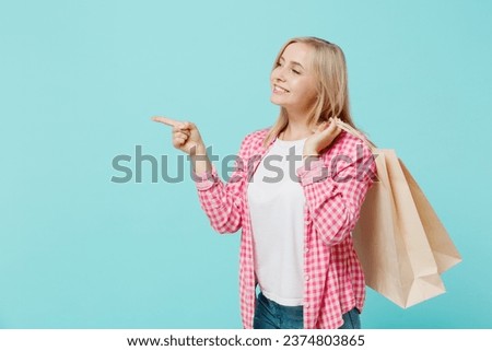 Young happy woman she 30s wears pink shirt white t-shirt holding package bags with purchases after shopping point index finger aside on workspace isolated on plain pastel light blue background studio.