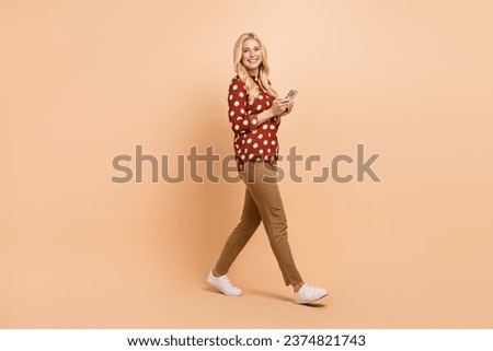 Full body profile portrait of lovely cheerful lady walking use smart phone isolated on beige color background