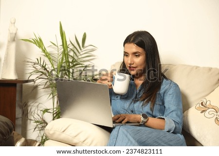 Portrait of a young happy female women sitting on the couch working on laptop with drinking cup of coffee and working on project at home. High quality photo