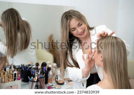 happy make-up artist working in the salon with young woman Royalty-Free Stock Photo #2374833939