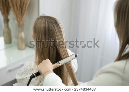 a hairdresser stylist using a Hair straightener to make woman's haircut Royalty-Free Stock Photo #2374834489