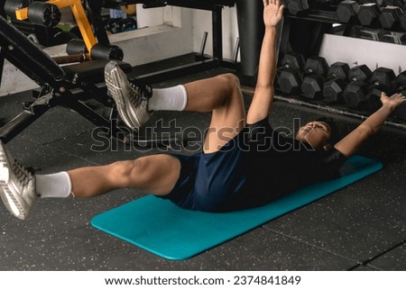 A young man doing a set of dead bug exercises lying on a mat. Leg and arm raised alternately. Abdominal and core workout at the gym. Royalty-Free Stock Photo #2374841849