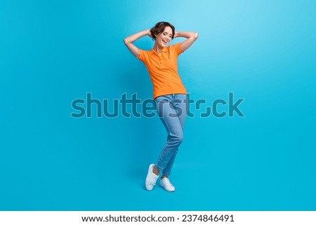 Full length photo of lovely pleasant woman wear orange t-shirt denim trousers hold arms behind head isolated on blue color background