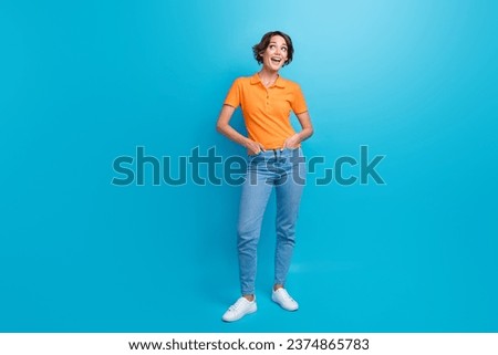 Full size photo of impressed girl dressed stylish polo jeans look at promo empty space arms in pockets isolated on blue color background