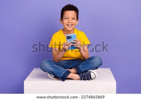 Full size photo of cute young schoolboy sit white platform hold device dressed yellow clothes isolated on violet color background