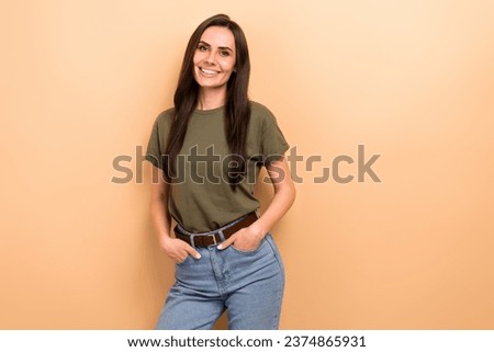 Photo of toothy beaming woman with straight hairdo dressed khaki t-shirt standing hold arms in pockets isolated on beige color background