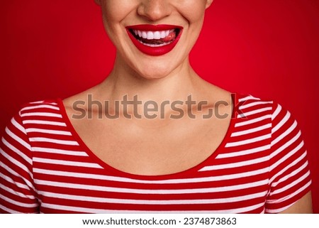 Cropped close portrait of young lovely lady showing perfect smile licking teeth wearing striped t shirt isolated on red color background