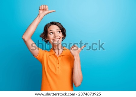 Photo of dreamy cheerful girl dressed orange polo looking showing two thumbs empty space isolated blue color background