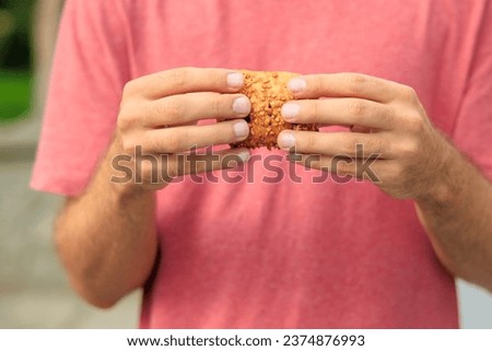 A guy's hand holds a sweet pastry with jam, snack and fast food concept. Selective focus on hands with blurred background and copy space for text.