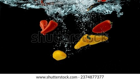 Red and Yellow Sweet Peppers, capsicum annuum, Vegetable falling into Water against Black Background