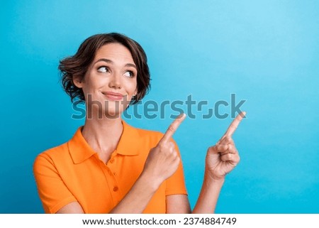 Photo of dreamy charming girl dressed orange polo showing two fingers looking empty space isolated blue color background