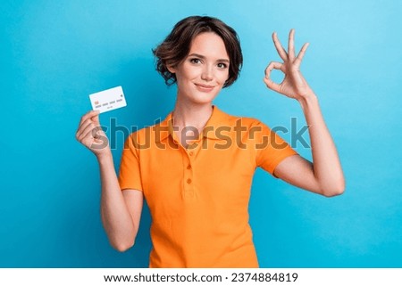 Photo of positive confident lady wear orange t-shirt rising credit card showing okey gesture isolated blue color background