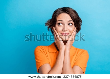 Photo of thoughtful girly girl dressed orange polo arms cheeks looking empty space isolated blue color background