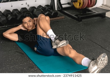A young man doing a set of bicycle crunches on a mat. Abdominal and core workout exercise at the gym. Royalty-Free Stock Photo #2374911425