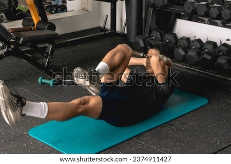 A young man doing a set of bicycle crunches on a mat. Abdominal and core workout exercise at the gym. Royalty-Free Stock Photo #2374911427