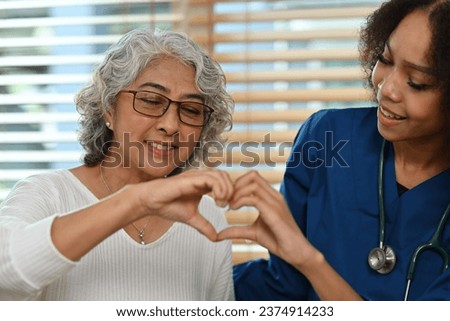 Portrait image of an old Asian woman and African nurse or caregiver making a heart shape with hands together, Care and health insurance for the elderly concept.