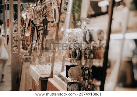 Indoor festive weekend market. Close up of hand made jewellery booth. Social pop up event in shopping mall for entrepreneurs and makers. Captured with tilt-shift lens. Selective focus; bokeh effect. Royalty-Free Stock Photo #2374918861