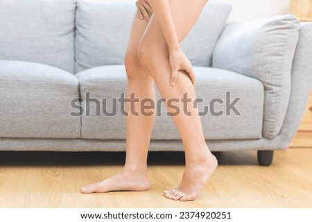 Muscle pain or leg pain, suffer asian young woman, girl hand massaging brawn leg calf muscle cramps or spasm, trauma from inflammation of tendon at calves while standing at home. Health care concept. Royalty-Free Stock Photo #2374920251