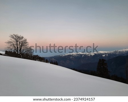 Landscape captured during trek to Kedarkantha peak in Garhwal Himalayas of Uttarakashi, Uttarakhand. Snow covered meadow slope, mountains and trees are in the photo. Horizon is pink and blue in color.