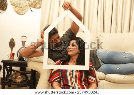 Happy couple holding paper home shape frame in living room and celebrating moving to new home. Concept - Luxurious lifestyle Real Estate in India.