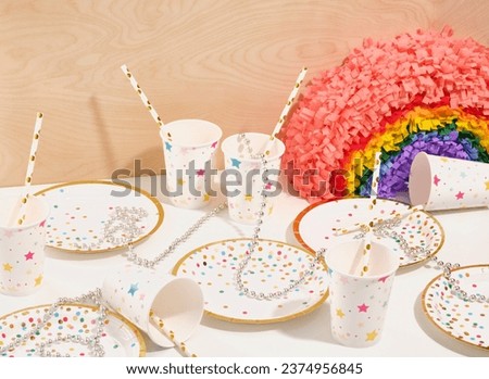 Celebrate table on a birthday party. Holiday plates confetti and paper cups with pictures of stars, colorful pinata rainbow.