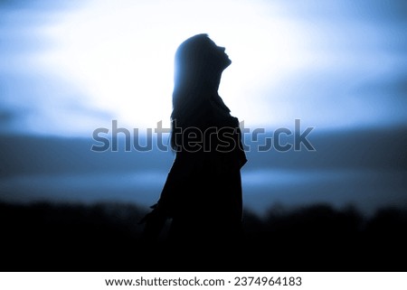 Youth woman soul at blue sun meditation awaiting future times. Silhouette in front of sunset or sunrise in summer nature. Symbol for healing burnout therapy, wellness relaxation or resurrection