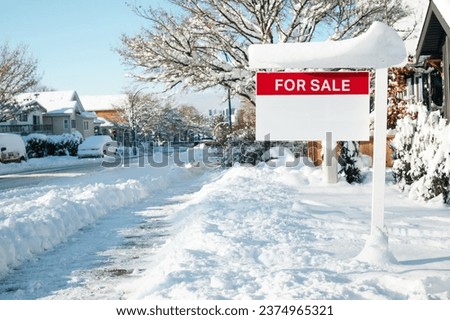 Home for sale sign with winter background scene on a sunny day. Red for sale realtor signage on sign post defocused snowed cars, homes and  street. Real estate and working in winter. Selective focus.