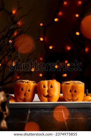 Stuffed peppers carved into pumpkins. Orange colorful peppers. Dinner. Halloween spirit. Fall. Orange lights. Festive. October food. Spooky food photography.  Royalty-Free Stock Photo #2374975855