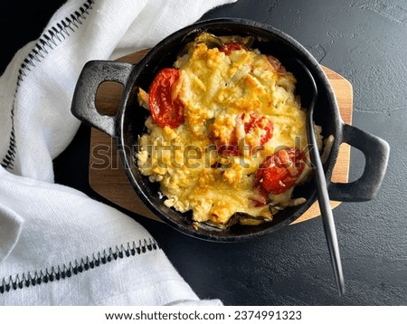 Greek dish with cheese, pepper and tomato: bouyourdi. Aerial picture of a cast iron cheesy dish, appetising and inviting, another staple for the Greek cuisine. Minimal dar background 