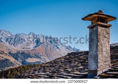 Mountain, chimney and stone tile roof in autumn. Liddes, Valais Canton, Switzerland.