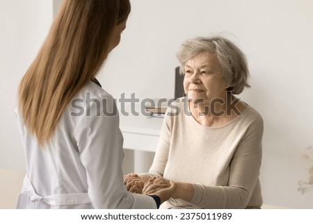 Older woman visit to doctor for medical checkup in hospital. Caring young therapist in white uniform holding hands of patient inform good news about treatment, support encouraging old person. Medicare Royalty-Free Stock Photo #2375011989