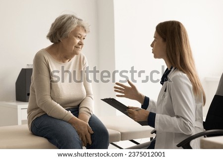 Female therapist in uniform talking to elderly retiree woman, asks about illness, gives professional medical help. Senior patient tells about health complaints at visit in clinic. Check-up, medicine
