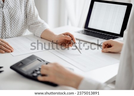 Accountant using a calculator and laptop computer for counting taxes with a client or a colleague at white desk in office. Teamwork in business audit and finance