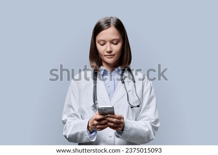 Young woman doctor, medical student with smartphone on grey background Royalty-Free Stock Photo #2375015093