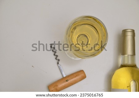 Unopened bottle of white wine with blank label, empty wineglass bunches of grapes, corkscrew and cork on white table background. Expensive bottle of chardonnay concept. Copy space, top view, flat lay