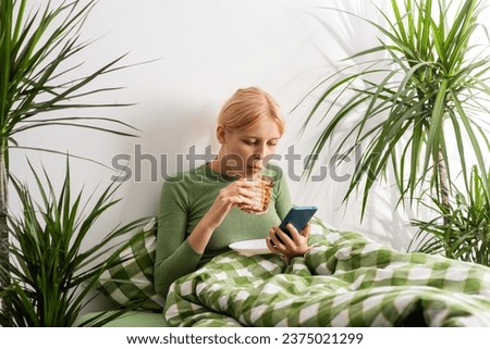 A girl deteriorates mentally, lying in bed all day, spending her time in bed with a phone, munching on toast. Bed rotting Royalty-Free Stock Photo #2375021299
