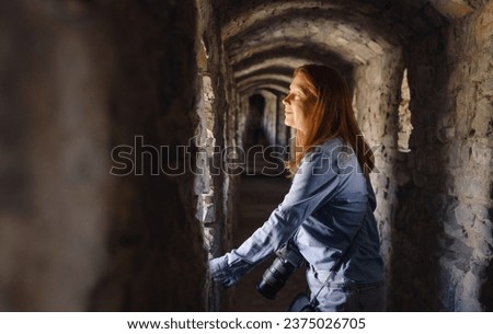 Woman walking through old tunnel, looking in window and taking pictures. Female visiting castle. Traveling in ancient building 