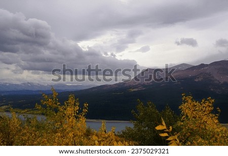 Billowing rainclouds loom over this Autumn scene near Glacier National Park, Montana.  Lower Two Medicine Lake is framed by trees in Fall colors while Lookout Point can be seen against the gloomy sky. Royalty-Free Stock Photo #2375029321