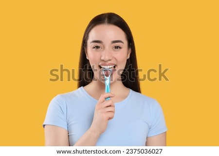 Happy woman brushing her tongue with cleaner on yellow background Royalty-Free Stock Photo #2375036027