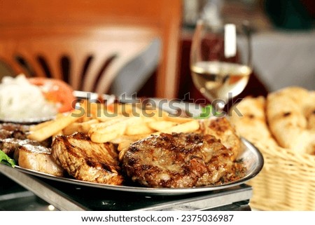 A barbecue plate with food, cevapcici, pomes frites, steaks, bread and glasses of wine in a homely restaurant atmosphere Royalty-Free Stock Photo #2375036987