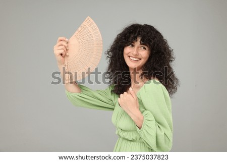 Happy woman holding hand fan on light grey background. Space for text