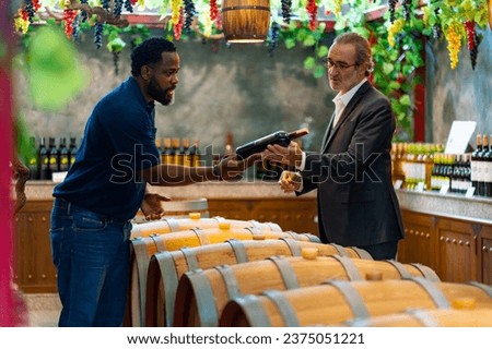 Professional African man wine shop worker explaining and recommending wine to customer at liquor store. Sommelier tasting wine in winery. Winery or brewery manufacturing industry and winemaker concept Royalty-Free Stock Photo #2375051221