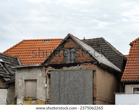 Old building ruin with boarded up door and window. The exterior is weathered and in very bad condition. The abandoned house is standing next to other buildings. Royalty-Free Stock Photo #2375062265