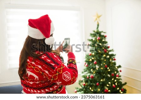Rear view of an obese woman with an ugly sweater and santa hat taking a picture of her beautiful christmas tree in her living room