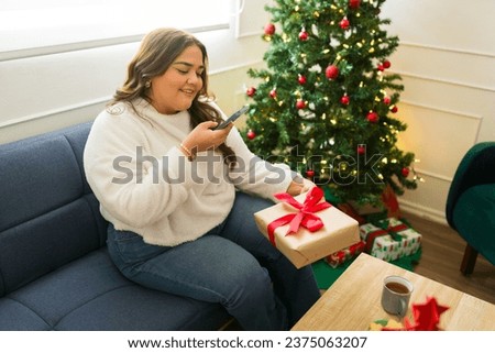 Attractive woman taking pictures with her phone for social media while opening christmas presents celebrating the holidays at home
