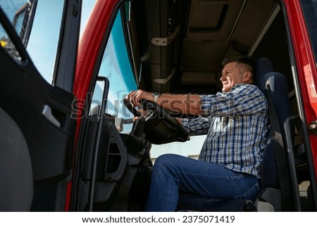 Caucasian man, truck driver sitting on driver seat with hands on the wheel, open door of truck  Royalty-Free Stock Photo #2375071419